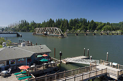 OR: Douglas County, Pacific Coast, Reedsport Area, Boardwalk, View over the Umpqua River towards the Coos Bay Rail Link steel truss drawbridge in open position; restaurant on the boardwalk [Ask for #274.533.]