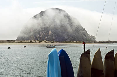 CA: South Coast Region, San Luis Obispo County, Pacific Coast Area, City of Morro Bay, Embarcadero, View across Morro Bay to Morro Rock, wreathed in clouds; rental kayaks. [Ask for #271.011.]
