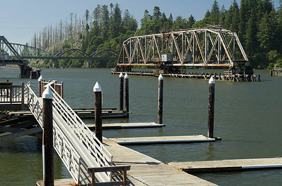 OR: South Coast Region, Douglas County, Pacific Coast, Reedsport Area, Town of Reedsport, Boardwalk, View over the Umpqua River towards the Coos Bay Rail Link steel truss drawbridge in open position; boat docks [Ask for #274.529.]