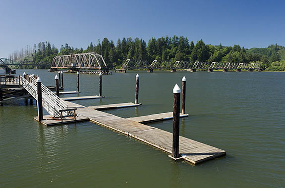 OR: South Coast Region, Douglas County, Pacific Coast, Reedsport Area, Town of Reedsport, Boardwalk, View over the Umpqua River towards the Coos Bay Rail Link steel truss drawbridge in open position; boat docks [Ask for #274.531.]