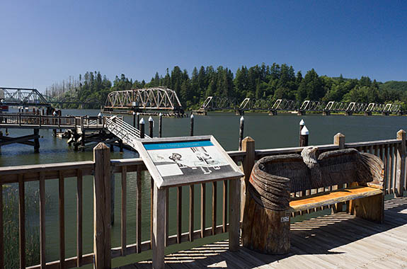 OR: South Coast Region, Douglas County, Pacific Coast, Reedsport Area, Town of Reedsport, Boardwalk, View over the Umpqua River towards the Coos Bay Rail Link steel truss drawbridge in open position; boat docks [Ask for #274.532.]