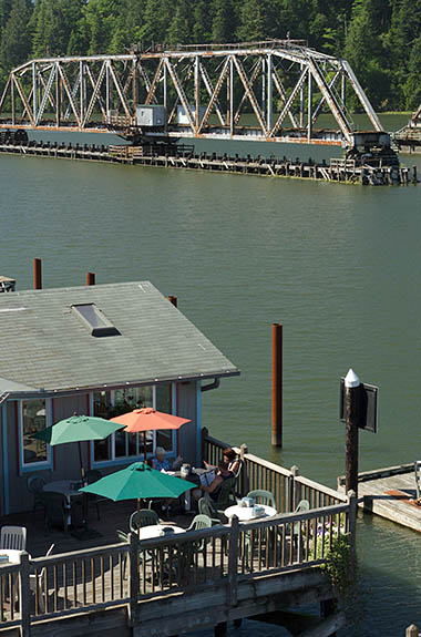 OR: South Coast Region, Douglas County, Pacific Coast, Reedsport Area, Town of Reedsport, Boardwalk, View over the Umpqua River towards the Coos Bay Rail Link steel truss drawbridge in open position; restaurant on the boardwalk [Ask for #274.534.]