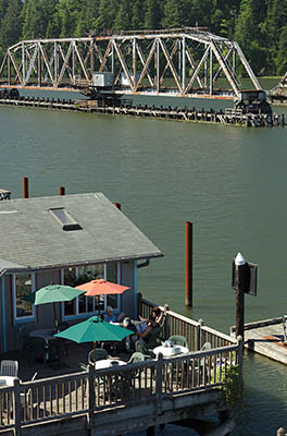 OR: Douglas County, Pacific Coast, Reedsport Area, Boardwalk, View over the Umpqua River towards the Coos Bay Rail Link steel truss drawbridge in open position; restaurant on the boardwalk [Ask for #274.534.]
