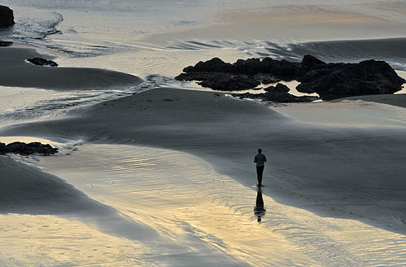 OR: South Coast Region, Coos County, Bandon Area, Town of Bandon, Devils Kitchen State Wayside, Clifftop view of a man on the beach enjoying the sunset, with sea spires surrounded by sand on the low tide [Ask for #278.041.]